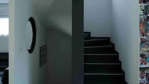Una scala con pavimento scuro e pareti bianche, che conduce a un pianerottolo con un quadro incorniciato e un elemento decorativo circolare a parete.