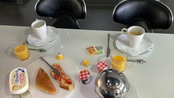 A breakfast table with a plate of toast, a glass of orange juice, a cup of coffee, a small container of butter, and a silver bowl.