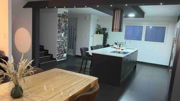 Una cucina moderna con isola centrale, mobili scuri e zona pranzo con tavolo e sedie in legno.