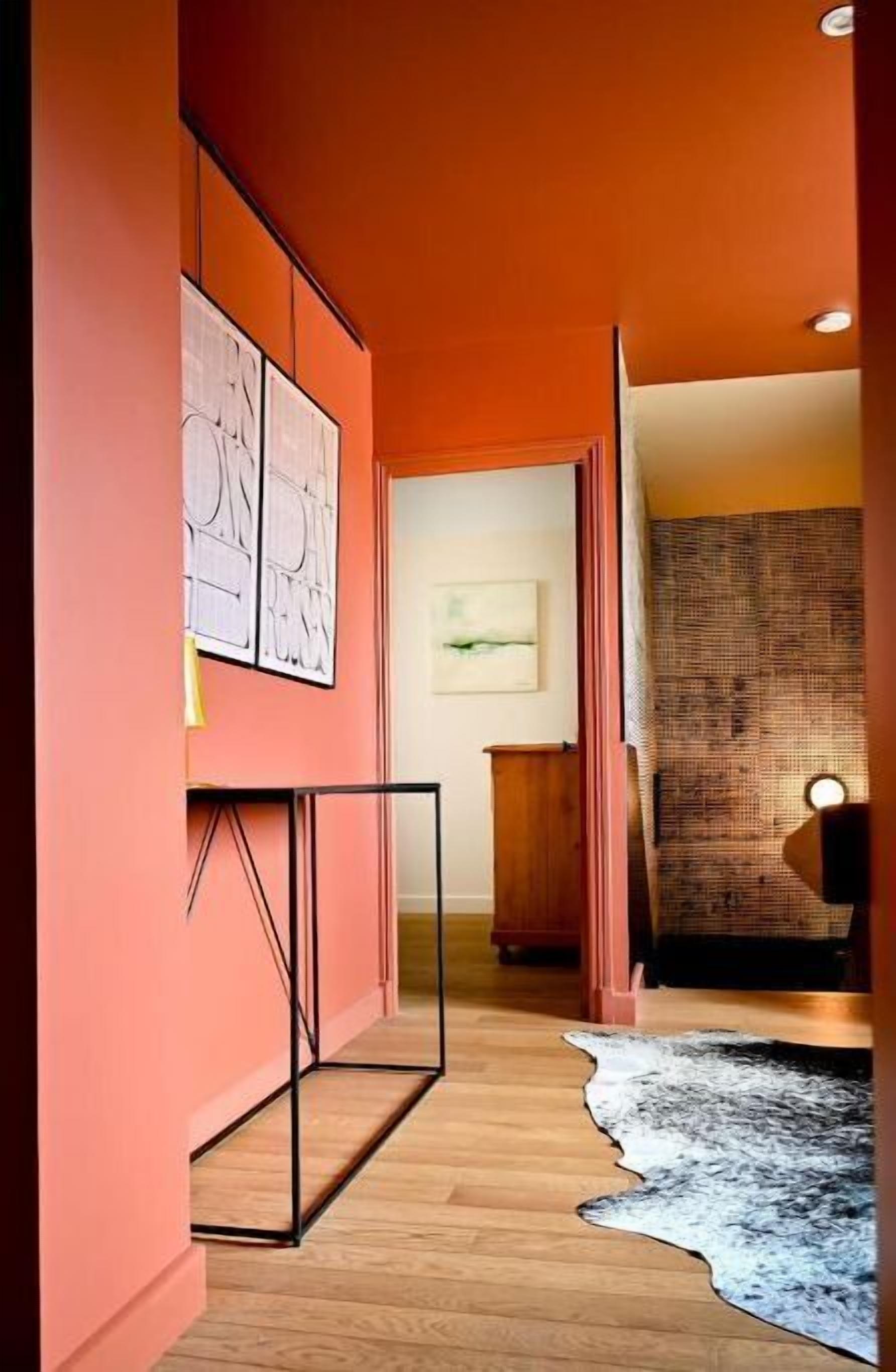 Un couloir doté d’un plancher en bois, une grande peinture abstraite sur le mur de gauche et un tapis à motifs sur le mur de droite.