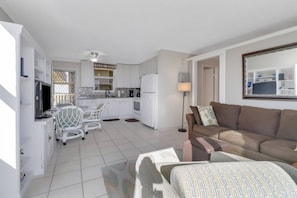 Un espacio habitable compacto con kitchenette, un comedor con televisor, un sofá y una lámpara.