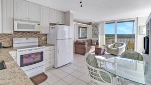 A modern kitchen with white appliances, a dining area with glass-top table, and a balcony with outdoor seating. - Beach & Tennis 1501 (Bonita Springs)
