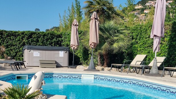 Une piscine d’un bleu éclatant, bordée de chaises longues et d’ombrelles, entourée de verdure et avec une colline en arrière-plan.
