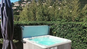 Un bain à remous avec des marches, un parasol et des chaises longues, le tout installé dans un jardin avec vue sur une colline.
