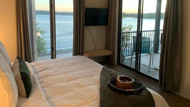 A hotel room with a large bed, a flat-screen TV, and a balcony with a view of the water. - Lakeside Boho Bungalow on Table Rock Lake (Kimberling City)