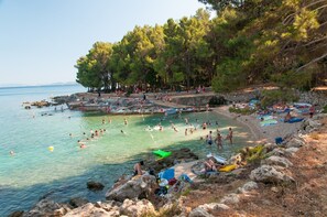 A beach with clear water, people swimming and sunbathing, and a rocky shoreline with trees.