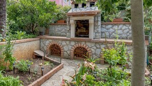 Un patio de piedra con una chimenea, rodeado por un jardín con diversas plantas y flores.