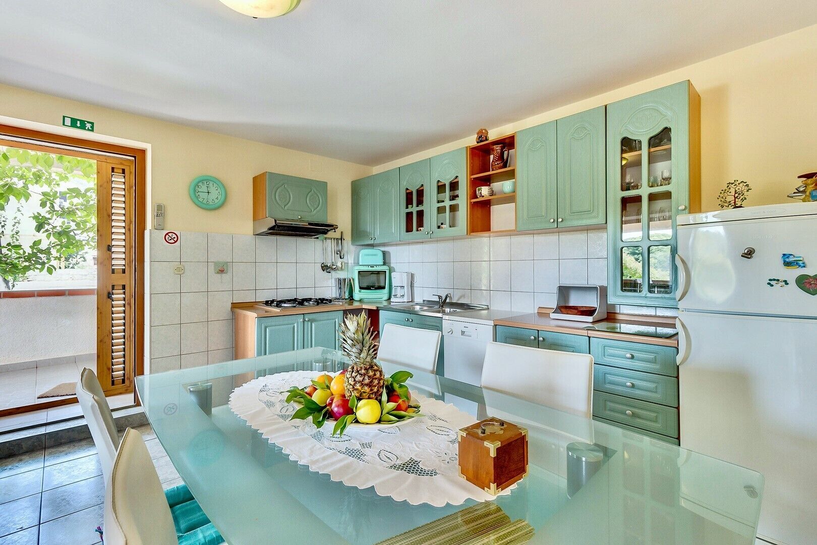Eine moderne Küche mit türkis-blauen Schränken, einem Glastisch und einem Kühlschrank.