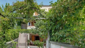 Un sendero estrecho que lleva a un edificio con una escalera y un pequeño jardín con plantas en macetas y una estatua de un cisne blanco.