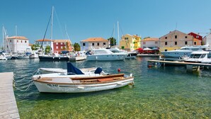 Un puerto deportivo con barcos amarrados, agua cristalina y edificios coloridos al fondo.