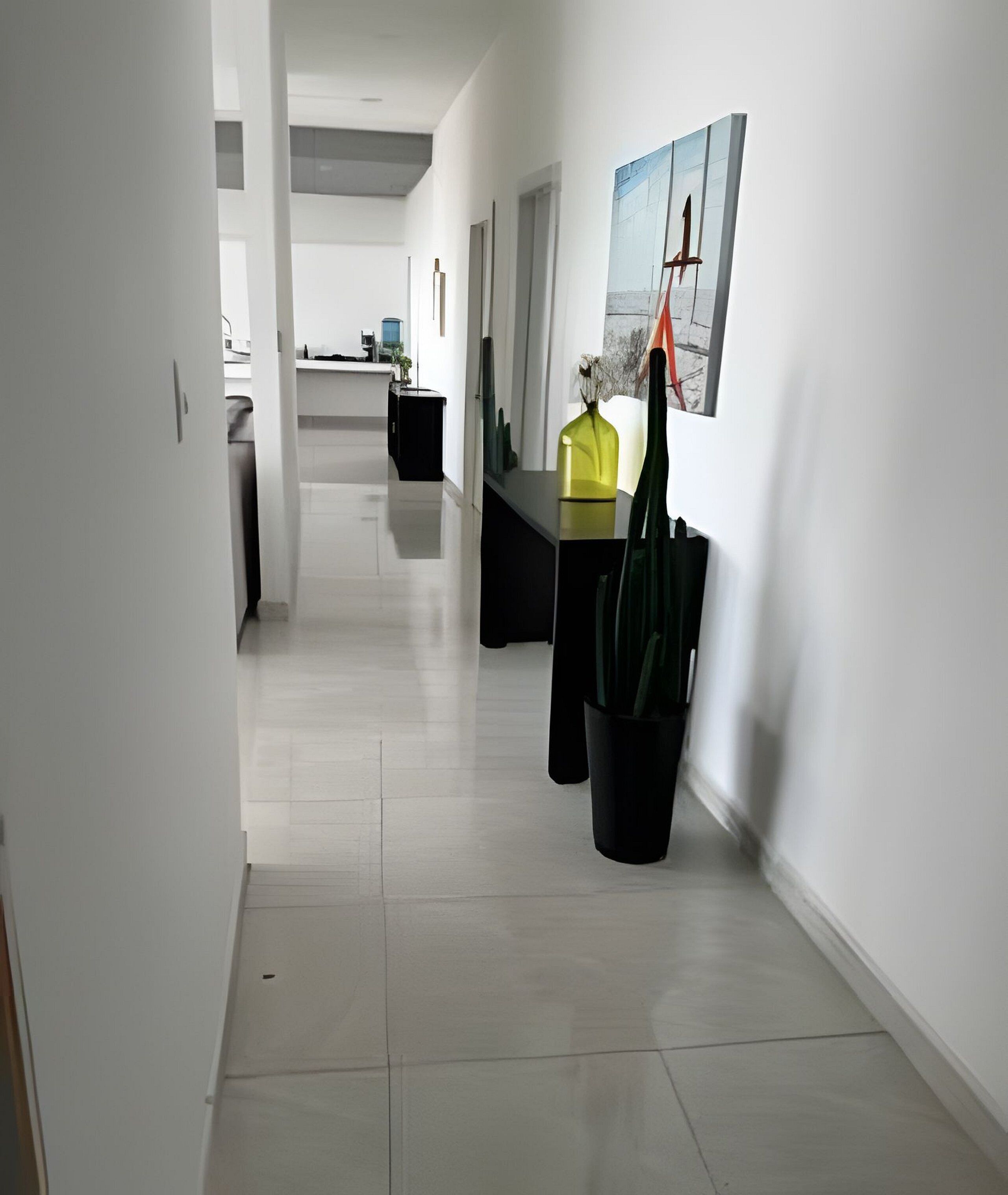 Un pasillo moderno con una zona de cocina al fondo, que incluye una mesa de comedor y sillas, y una planta en maceta.