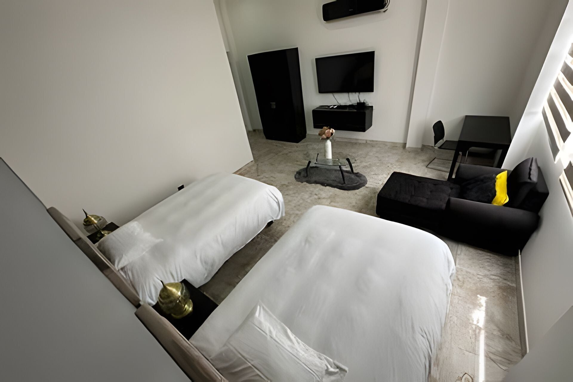 A hotel room with two beds, a black sofa, a small table, and a TV mounted on the wall.