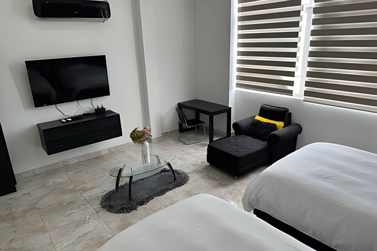 A modern hotel room with a flat-screen TV, a small table, a sofa, and a bed.