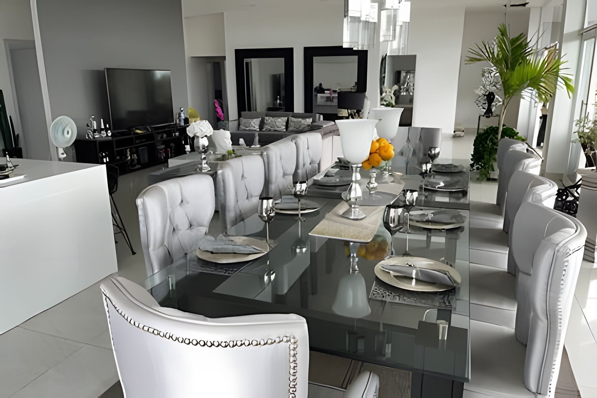 Un comedor moderno con una mesa de cristal, sillas blancas tapizadas y un jarrón central con flores.