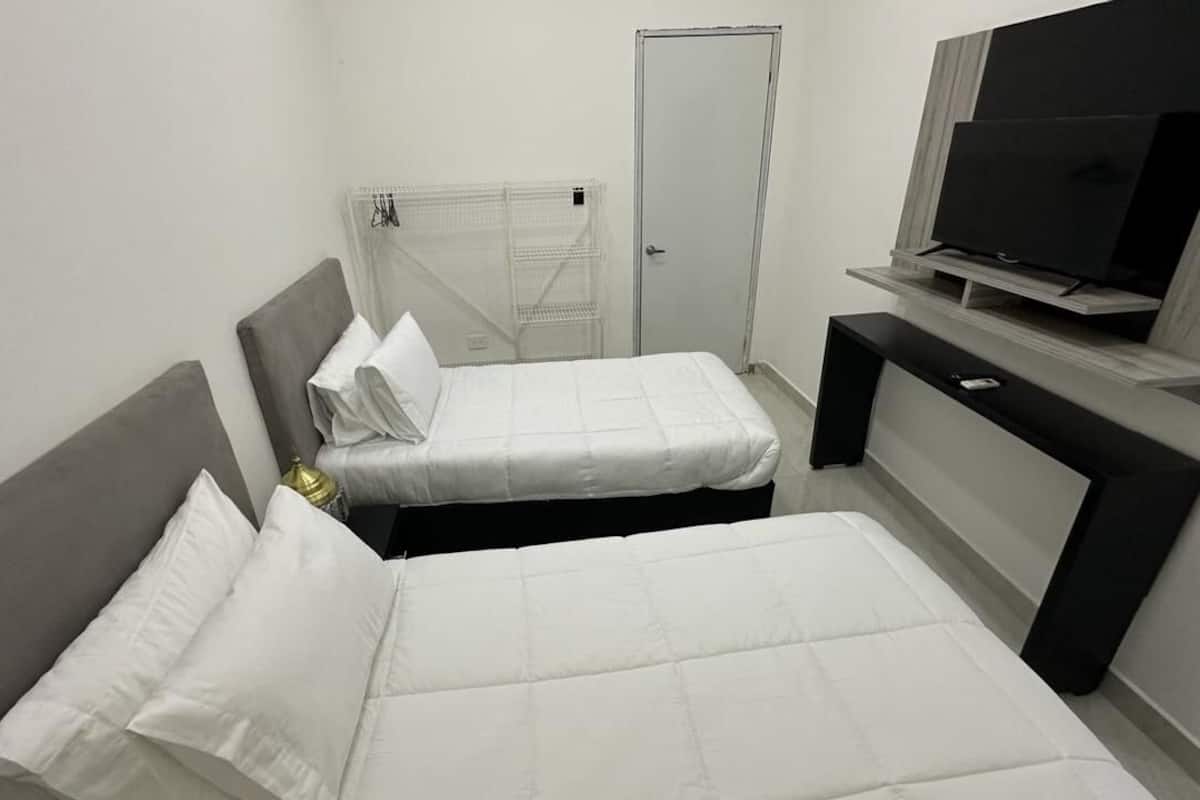 A hotel room with two beds, a TV on a stand, a wardrobe, and a small table.