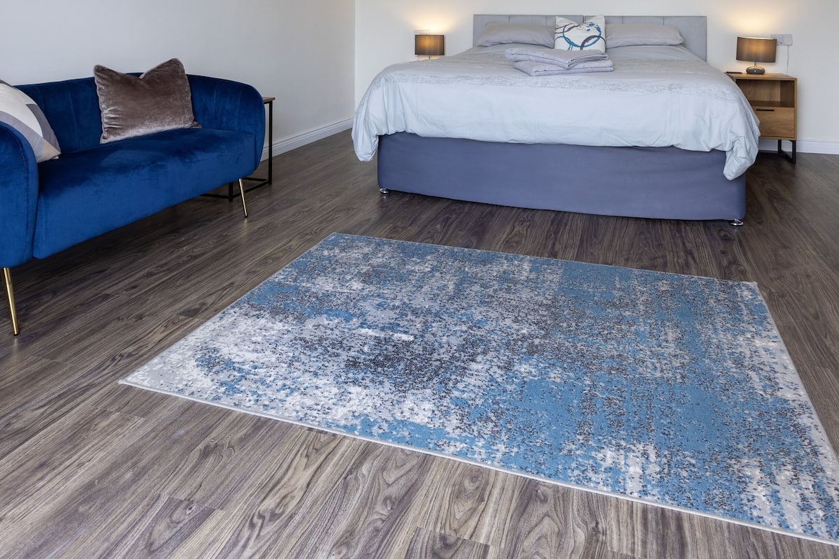 Une chambre à coucher avec un lit, un canapé bleu, une table de chevet et une lampe sur pied.