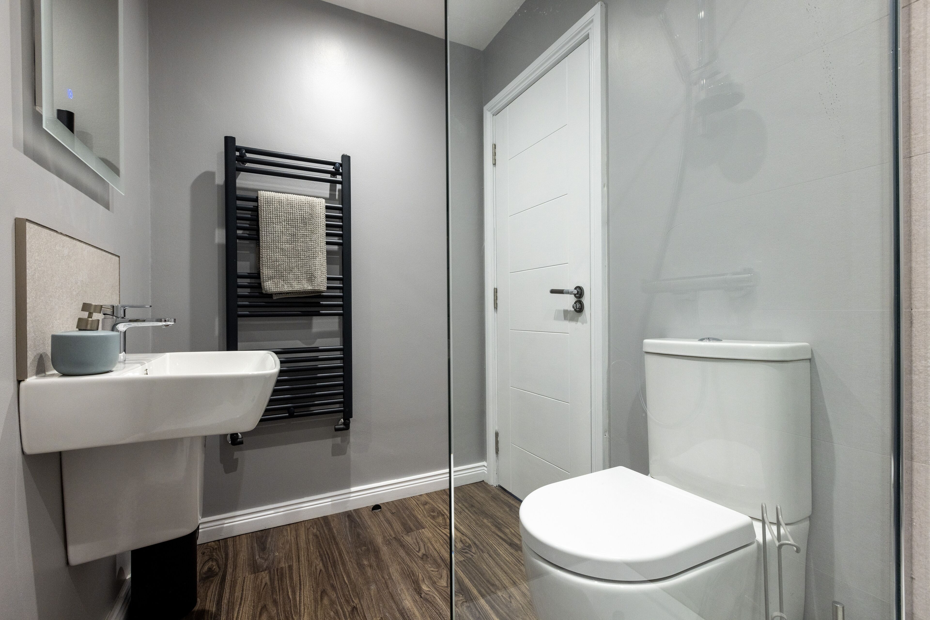 A modern bathroom with a white sink, black towel rack, and a white toilet.