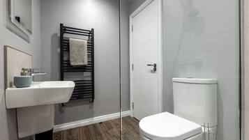 A modern bathroom with a white sink, black towel rack, and a white toilet.