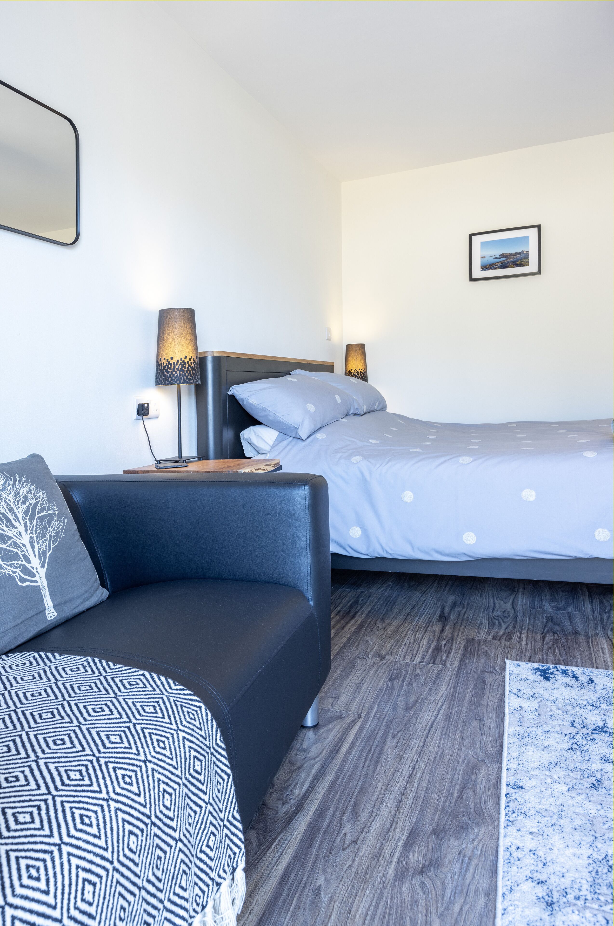 A modern bedroom with a bed, a sofa, a nightstand, and a lamp.