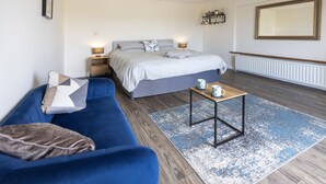Une chambre à coucher avec un lit, un canapé bleu, une petite table avec une tasse, et un grand miroir au mur.