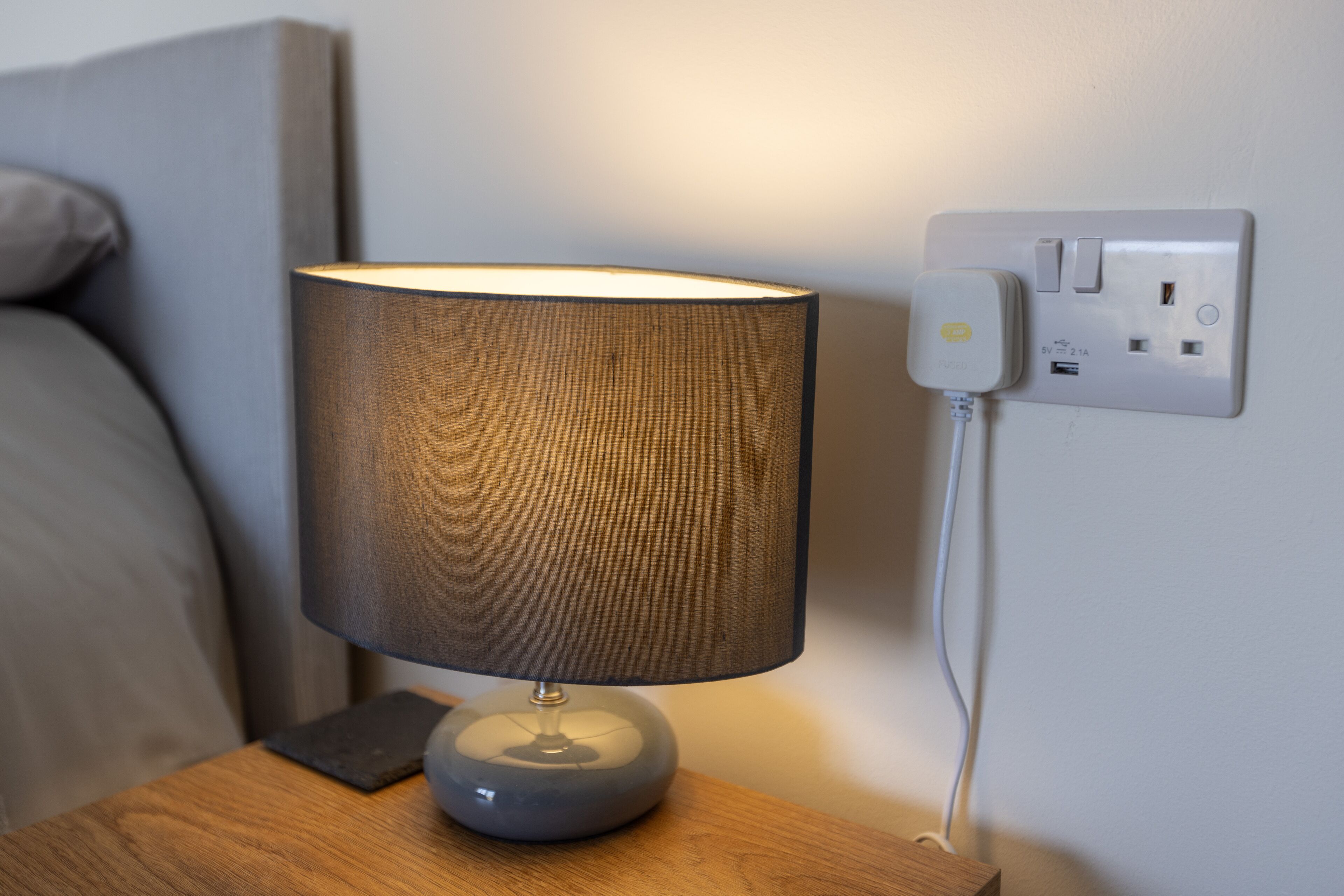 Een nachtkastje met een lamp, een stopcontact en een wandcontactdoos.