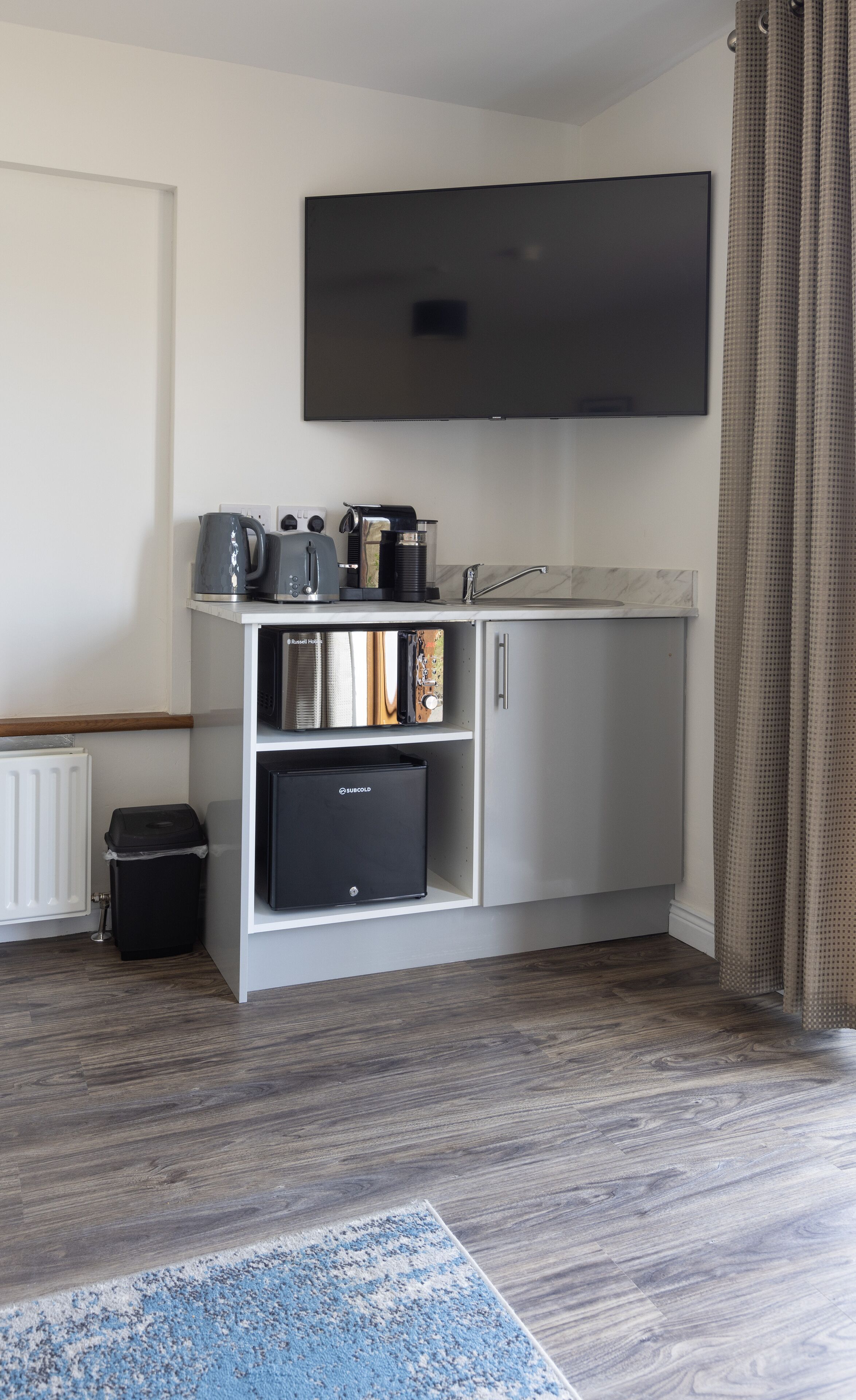 A modern kitchenette with a built-in TV, a coffee maker, and a mini-fridge.