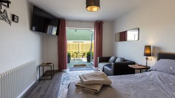 A hotel room with a bed, a TV, a sofa, a small table, a lamp, and a view of the outside.