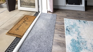 Un salon moderne doté d’une porte-fenêtre coulissante donnant sur un balcon, d’un téléviseur à écran plat fixé au mur, d’une kitchenette équipée et d’une plante en pot.