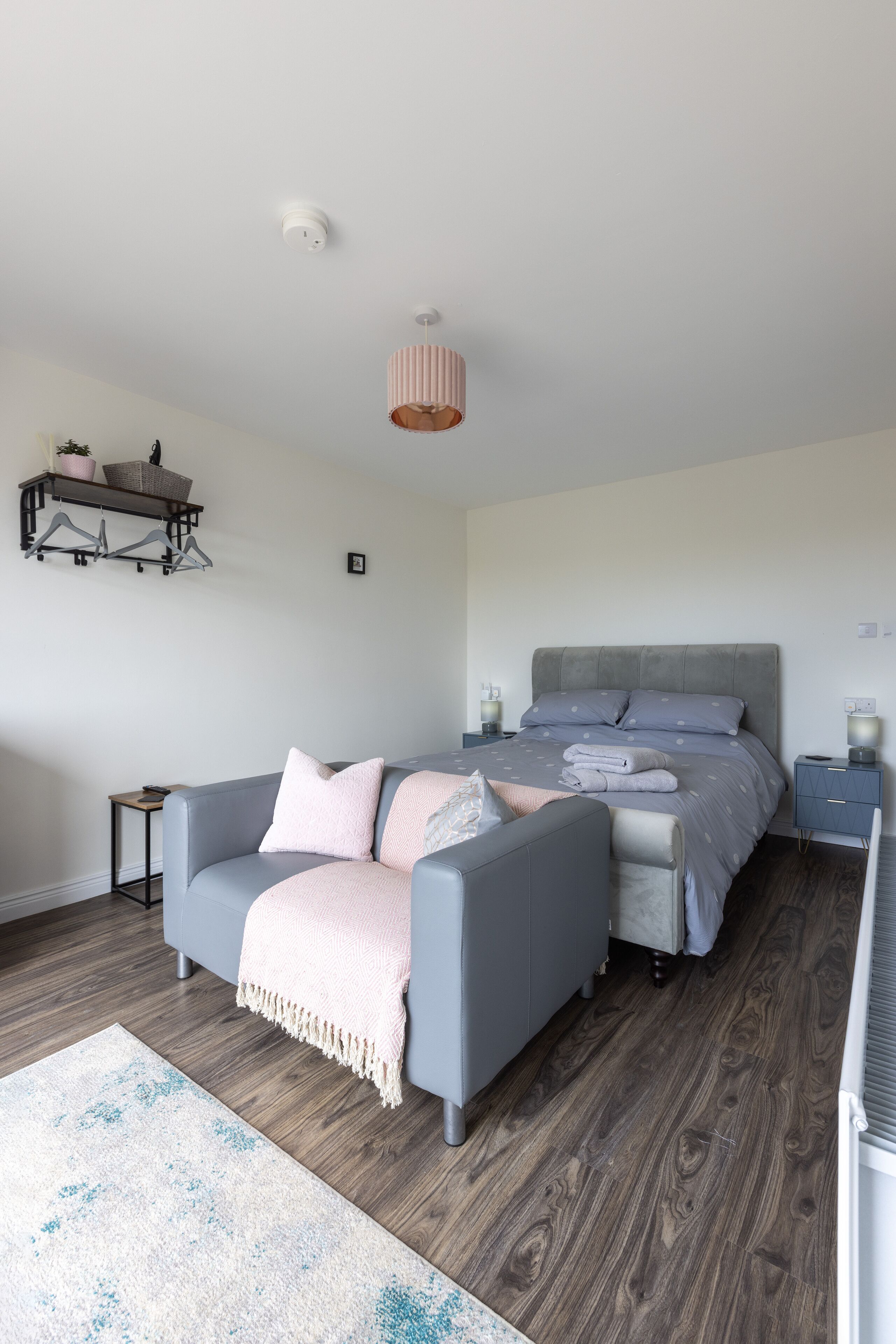 A modern bedroom with a grey sofa, a bed with a grey headboard, a bedside table, a small table, and a hanging light fixture.