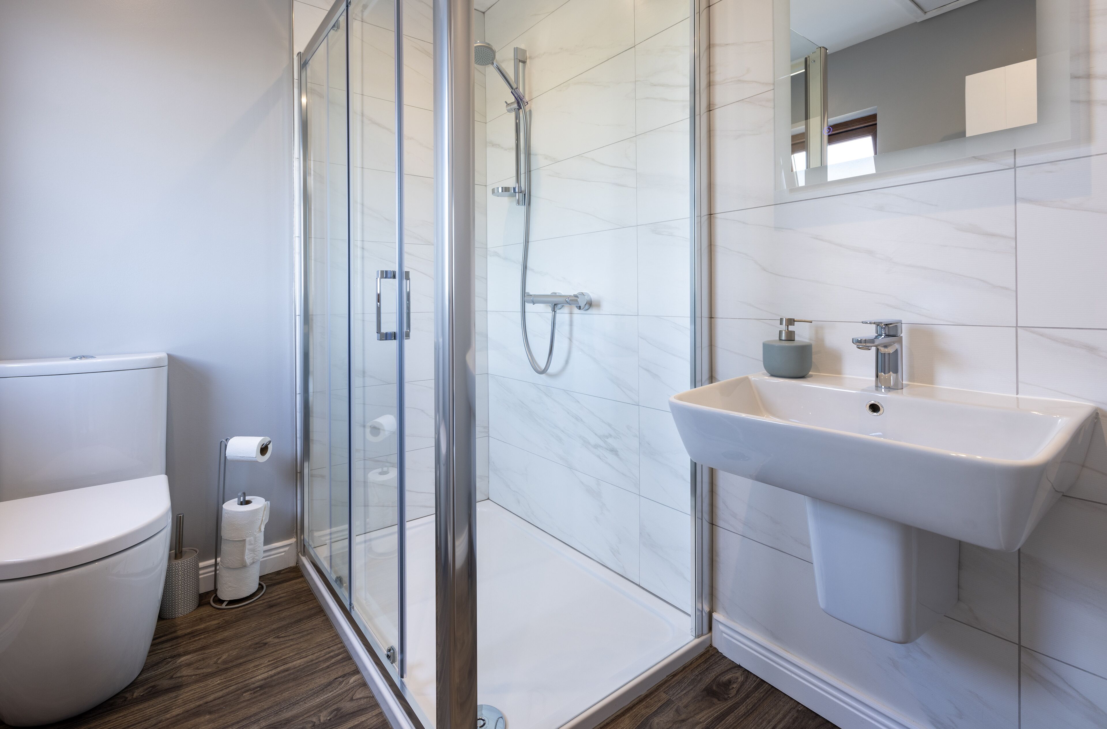 A modern bathroom with a glass-enclosed shower, a white sink, and a toilet.