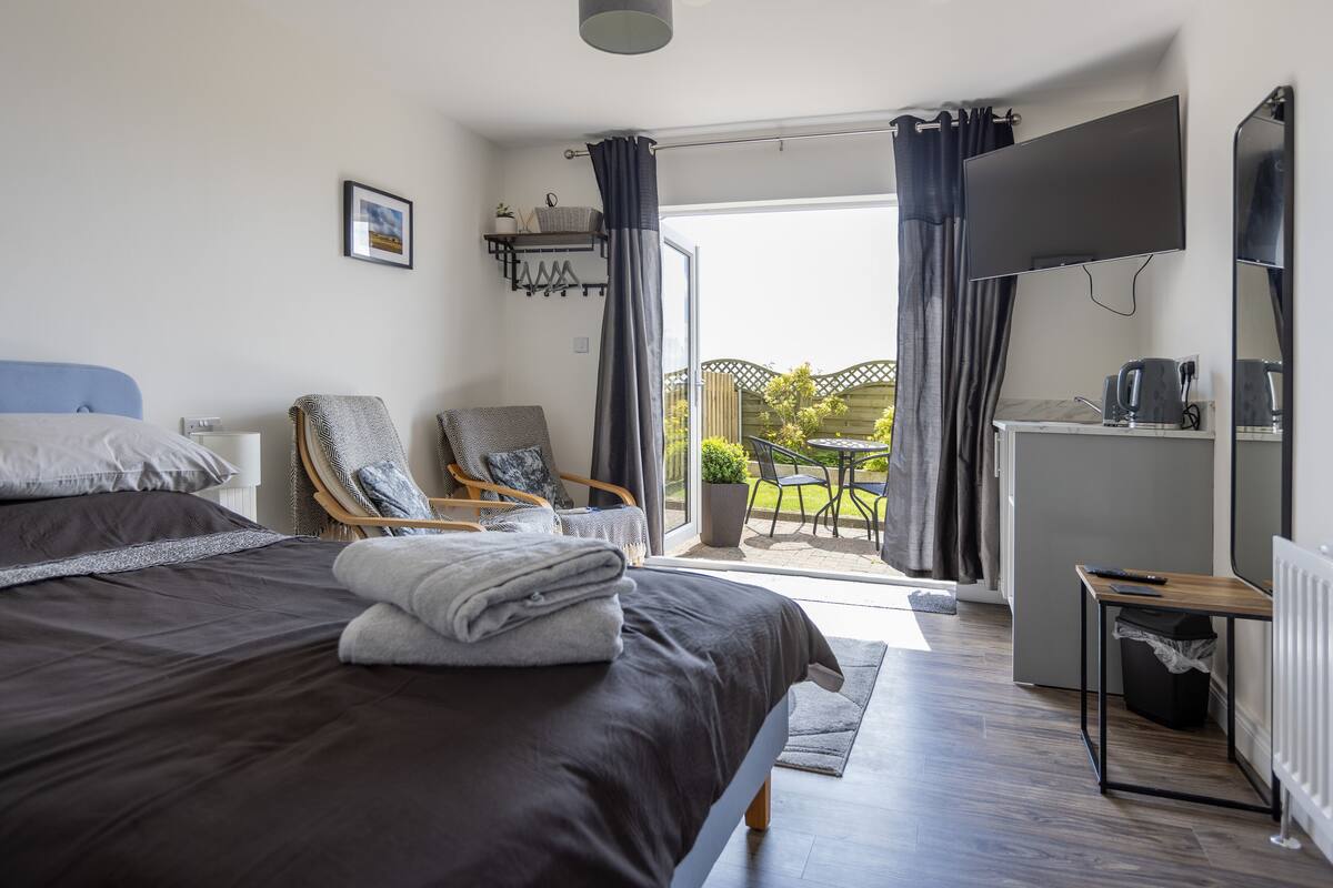 Une chambre moderne avec un grand lit, un fauteuil, une télévision et un balcon avec vue.