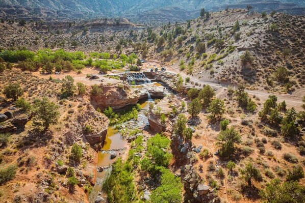 Een natuurlijk landschap met een waterval, rotsachtig terrein, schaarse begroeiing en een onverharde weg.
