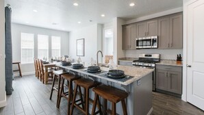 A modern kitchen with a central island, bar stools, and a dining area with a long table and chairs. - 30 people with pool, waterslide and pickleball (Washington)