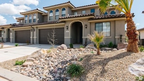 A two-story house with a garage, a landscaped front yard with rocks and a palm tree, and a clear blue sky. - 30 people with pool, waterslide and pickleball (Washington)