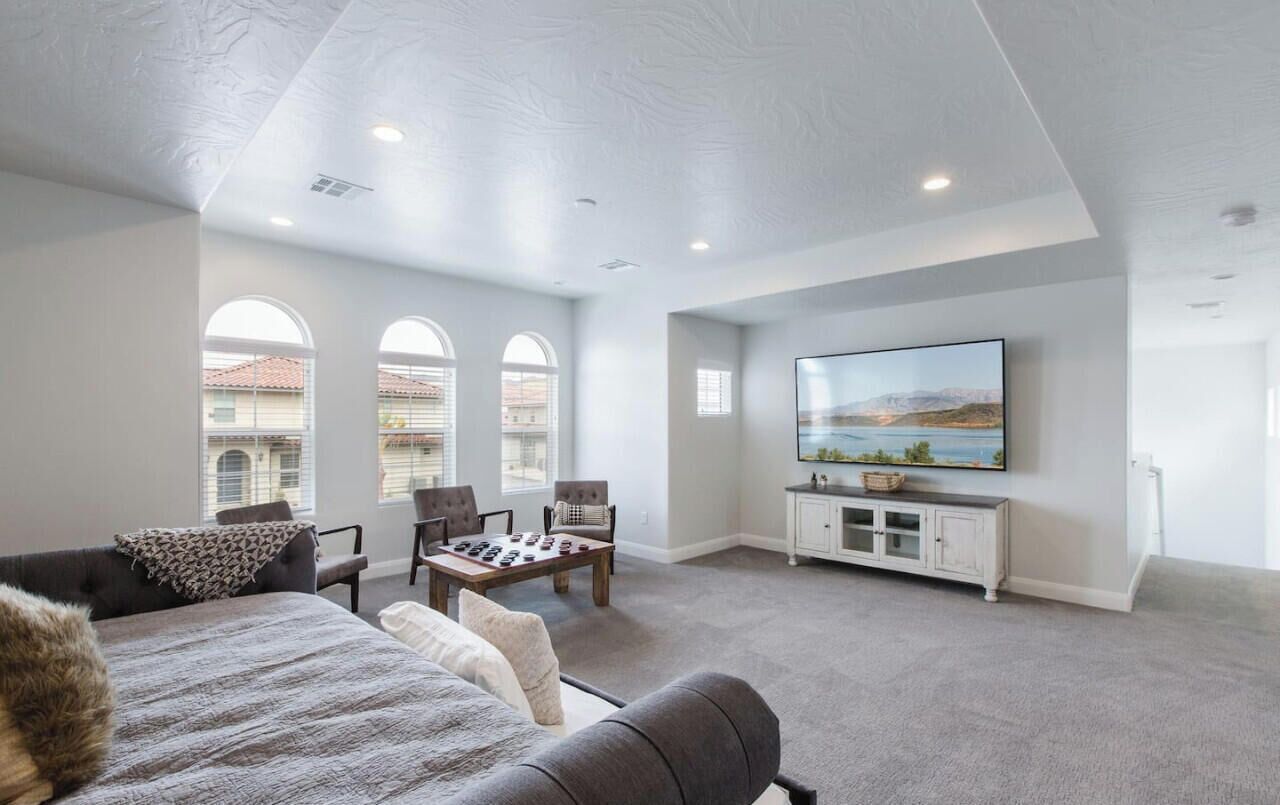 A spacious living room with a large TV, comfortable seating, and a view of the city through arched windows.