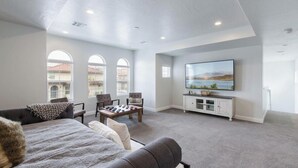 A spacious living room with a large TV, comfortable seating, and a view of the city through arched windows. - 30 people with pool, waterslide and pickleball (Washington)