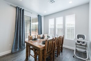 Un comedor con una mesa y sillas de madera, una trona y vistas a través de un ventanal.
