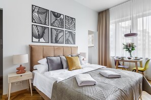 Ein ordentlich eingerichtetes Hotelzimmer mit einem großen Bett, einem Nachttisch mit Lampe, einem kleinen Tisch mit Blumenvase und einem Sessel.