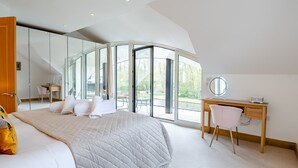A bedroom with a large bed, a desk, and a chair. - This stunning waterside home offers an amazing space for families and friends. (Wroxham)