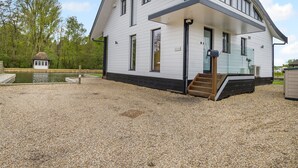 A modern two-story house with a covered porch, a small dock, and a gravel driveway. - This stunning waterside home offers an amazing space for families and friends. (Wroxham)