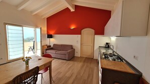 A compact living space with a kitchenette, a sofa, a dining table with chairs, and a large window with a view.