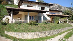 A two-story house with a stone retaining wall, a covered porch, and a view of a mountainous landscape.