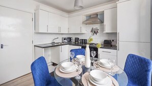 A modern kitchen with white cabinets, a dining table set with plates and glasses, and a blue chair.