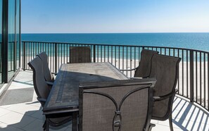 A terrace with a table and chairs, overlooking a beach and the sea.