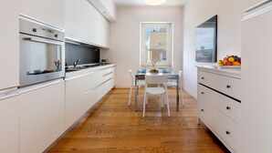 Une cuisine moderne avec des meubles blancs, un four encastré et un coin repas comprenant une table et des chaises blanches.
