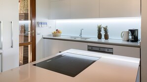 Una cocina moderna con armarios blancos, horno empotrado, lavabo y encimera con cafetera y dos piñas.