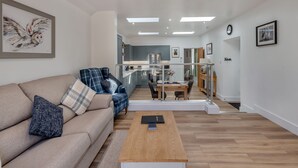 A modern living room with a sofa, coffee table, and a dining area with a glass partition. - 1 bedroom accommodation in Consett, County Durham (Consett, County Durham)