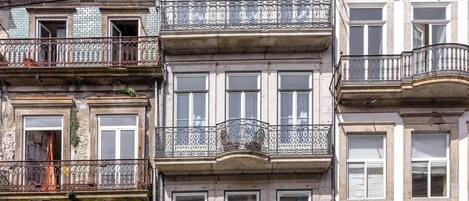 Un edificio de varios pisos con balcones, una tienda en la planta baja y un cielo despejado.