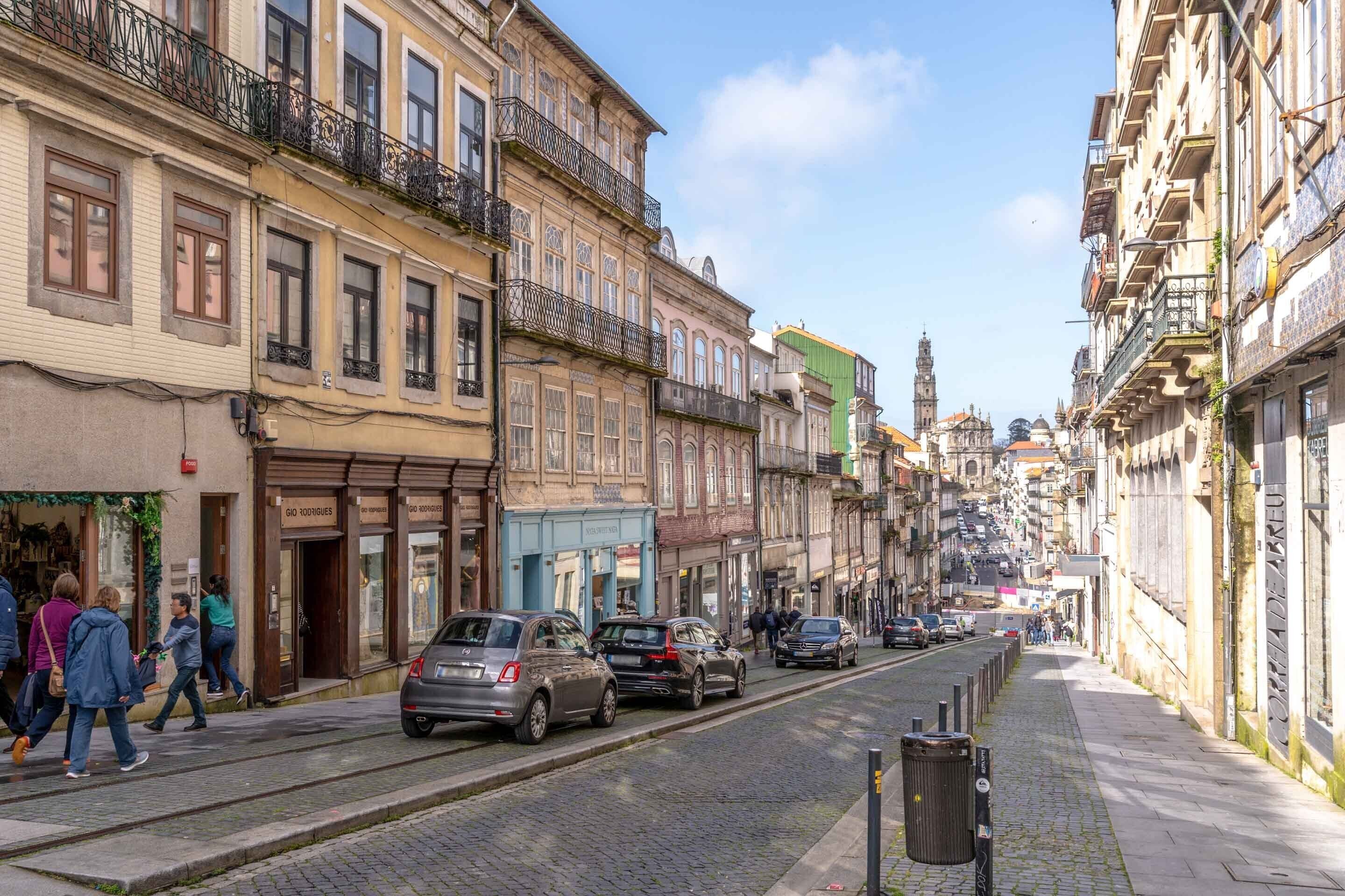 A cobblestone street lined with historic buildings, some with balconies and storefronts.