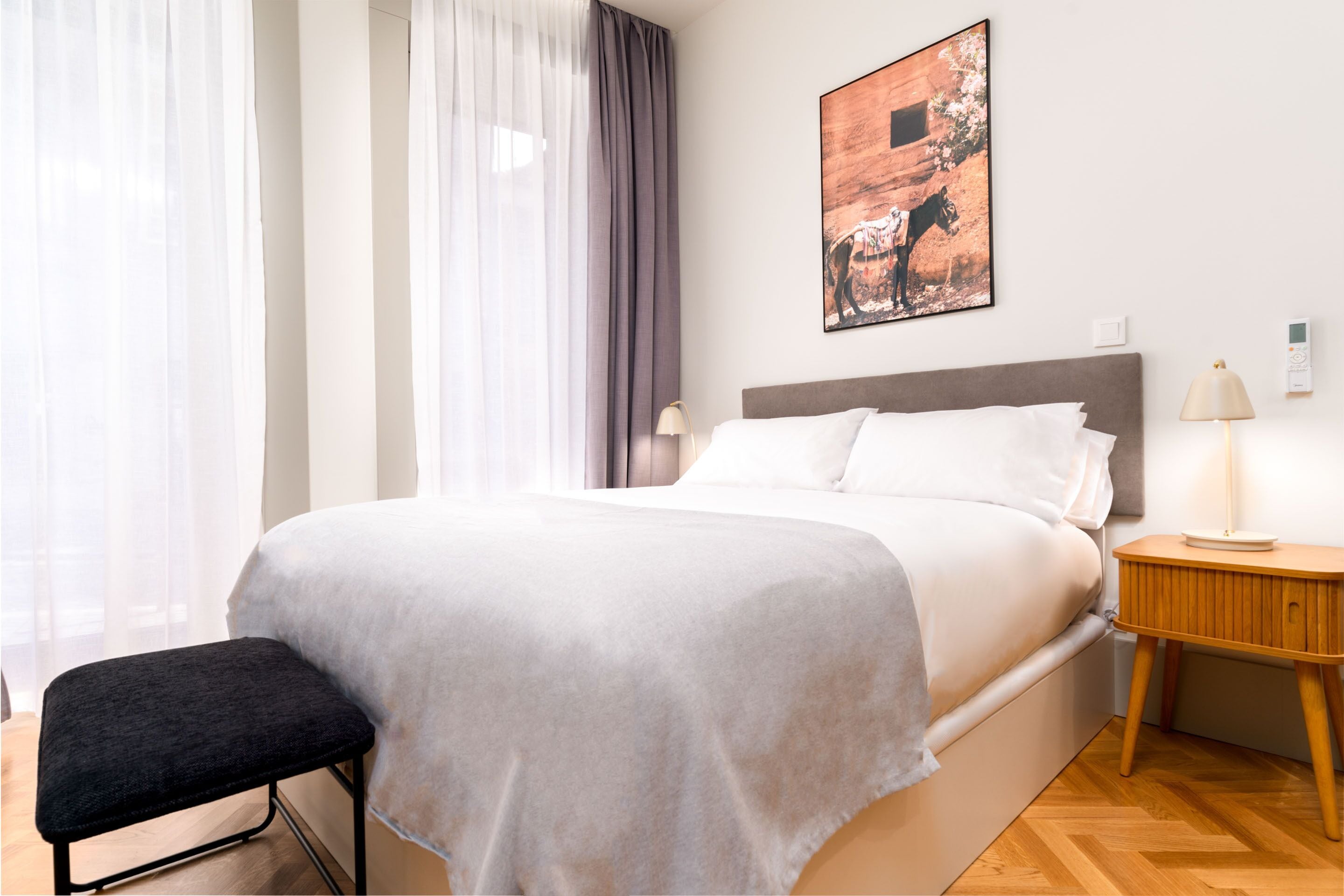 A neatly made bed with white linens, a wooden nightstand with a lamp, and a framed picture on the wall.